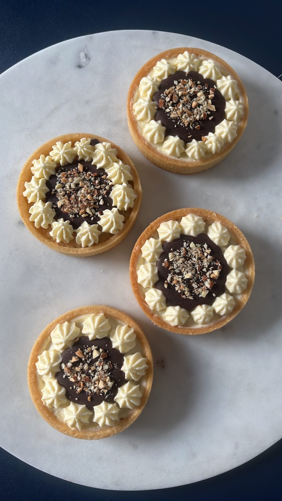 A chocolate tart with cream piped on top and almond pieces in the center